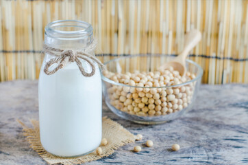 Closed up homemade soybean milk in glass over blur seeds in glass bowl on wooden background