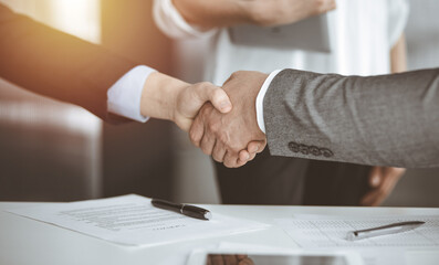 Obraz premium Business people shaking hands finishing contract signing in sunny office, close-up. Handshake and marketing
