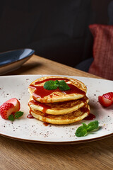 Stack of pancakes with of strawberry slices and caramel syrup on a wooden table.