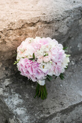 Beautiful bridal bouquet of white and pink flowers and greenery, on a gray textural background. Hydrangea wedding bouquet.