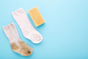 Baby socks and household soap on light blue table background. Pastel color. Detergent for clothes washing. Compare between dirty and clean socks. Problem and solution. Empty place for text. Top view.