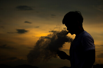Obraz premium Man smoke electronic cigarette outdoor on beautiful sky background during sunset.