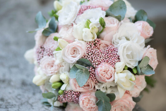 Close up of beautiful bridal bouquet of white and pink flowers and greenery, on a gray texture background. Wedding bouquet composed of roses, ozothamnus, freesia and lisianthus.