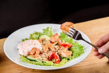 Salad with shrimps, quinoa, tomatoes, peppers, cucumber, lettuce, mayonnaise on white round plate on wooden table