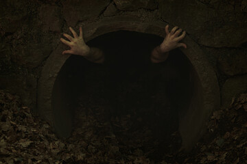 Small dark tunnel opening with two hands with twisted fingers poking out and holding to edge, someone trying to get out