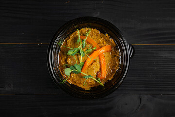 Hummus garnished with peppers and herbs in black plate on dark wooden table.