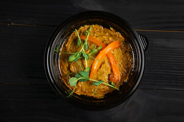 Hummus garnished with peppers and herbs in black plate on dark wooden table.