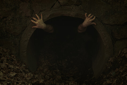 Small dark tunnel opening with two hands with twisted fingers poking out and holding to edge, someone trying to get out - Powered by Adobe