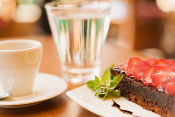 Chocolate cake, brownie with strawberries and mint, espresso, glass of water on a wooden table
