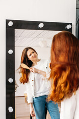 a girl of European appearance stands in front of a mirror, combs her hair with a comb, hair beauty, care,