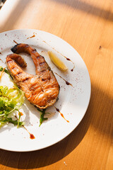 Grilled salmon steak with lettuce and lemon on white plate on wooden table