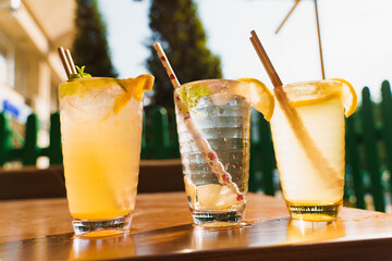 Cocktails with lemon and mint in glasses with tube on a wooden table against the background of a restaurant. Cold summer lemonade