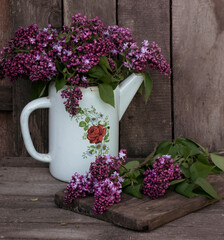 enameled coffee pot with a bouquet of lilacs on a background of old boards