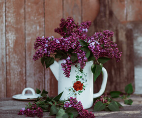 enameled coffee pot with a bouquet of lilacs on a background of old boards
