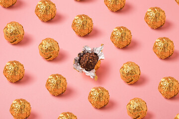 Chocolate balls in gold foil on pink background, pralines in open wrapper foil