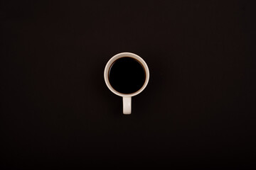 Top view of white ceramic mug with black coffee on black background.