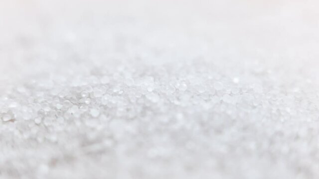 Close-up of salt in soft focus at high magnification. Salt granules fall onto a light surface.