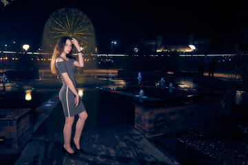 Cute sexy woman in a short dress near the city fountain in the night city.