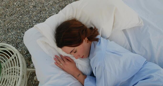 Ragazza bella con camicia azzurra dorme su un letto in spiaggia a baldacchino vicino al mare