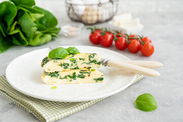 Omelette with spinach, green onions and feta cheese on a white plate on a gray concrete background. Healthy breakfast. Copy space.