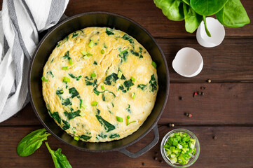 Omelette with spinach, green onions and feta cheese in a cast-iron frying pan on a dark wooden background. Healthy breakfast. Rustic style. Copy space.