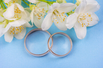 a pair of gold wedding rings with white jasmine flowers on a blue background close up