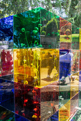Cubos agrupados de metacrilato transparente y de colores rellenos de plantas y donde se reflejan transeúntes.