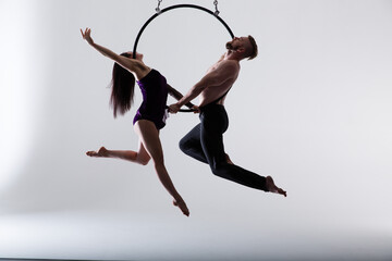 Couple of beautiful aerial gymnasts from Ukraine "Duo lotos" flying on fabric ropes and circle, performing aerial exercise with white fabrics on white background