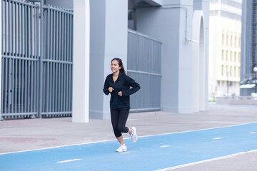 Fototapeta na wymiar Asian Beautiful Young woman black suit with happy running or jogging on blue running track in the day time. exercise, training, fitness, workout, sport, lifestyle and healthy concept.