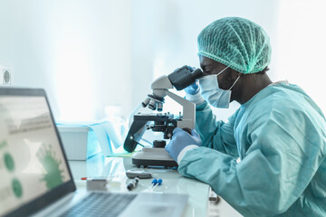 African doctor working in research laboratory examining microorganisms through microscope - Science...