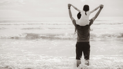 Little child girl riding on dads neck. Father and daughter standing on beach. Concept of Fathers...