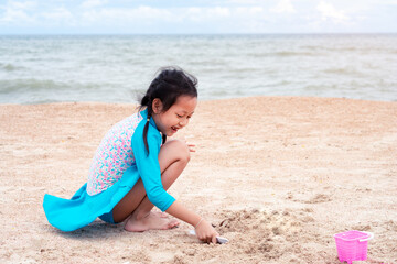 Happy little girl playing with sand on tropical beach