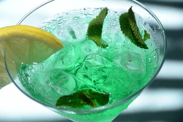 Glass of cocktail green fairy with lemon and mint leaves. Sweet refreshing mint liqueur, with ice and absinthe, rum, Ice cubes and Vodka