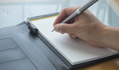 A hand of a man holding a pen . A person writing a notebook. memo. Writing on a paper.