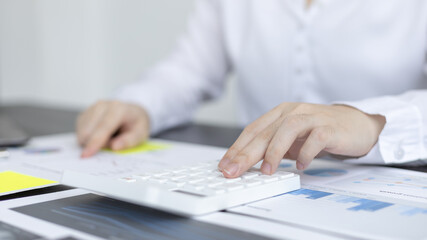 Fototapeta premium Young Asian businesswoman presses a calculator to calculate income tax and corporate income in a private office, Finance, Accounting, Tex, Statistical graphs of marketers investing in real estate.