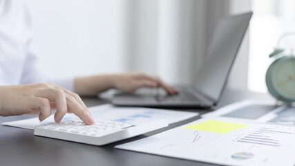 Young Asian businesswoman presses a calculator to calculate income tax and corporate income in a private office, Finance, Accounting, Tex, Statistical graphs of marketers investing in real estate.