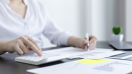 Young Asian businesswoman presses a calculator to calculate income tax and corporate income in a private office, Finance, Accounting, Tex, Statistical graphs of marketers investing in real estate.