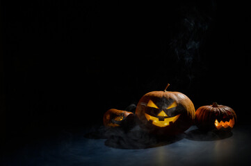 Pumpkins with carved grimaces and candles inside in the dark for halloween. Jack o latern in smoke.