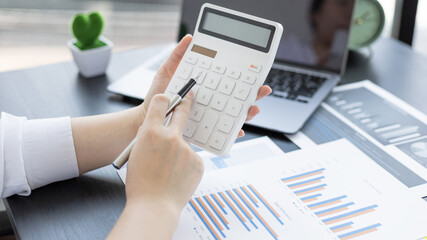 Young Asian businesswoman presses a calculator to calculate income tax and corporate income in a private office, Finance, Accounting, Tex, Statistical graphs of marketers investing in real estate.