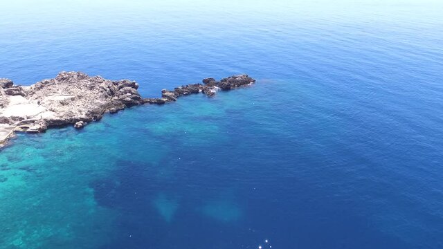 Une vid&eacute;o a&eacute;rienne avant au dessus d'une eau turquoise et limpide dans une destination paradisiaque m&eacute;diterran&eacute;enne. Passage d'oiseaux dans le paysage et proche des rochers 
