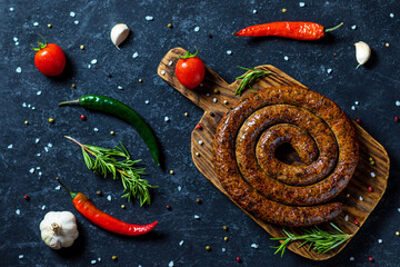 Snail sausage baked in an old oven is on a wooden board with pepper , garlic and rosemary.