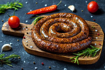 Spiral grilled sausages on wooden serving board.