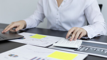 Financial or accounting professionals use a laptop to analyze the company's revenue-expenses graph to prepare for presentation to the chief executive and partner, Calculate data with a calculator.