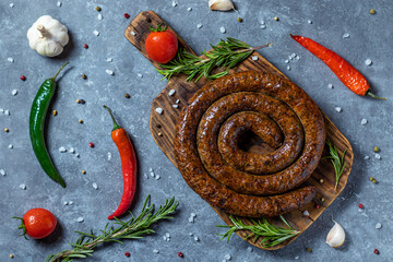 Smoking sausage on wooden board with vegetables and spices .