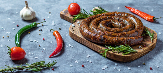 Snail sausage baked in an old oven is on a wooden board with pepper , garlic and rosemary.
