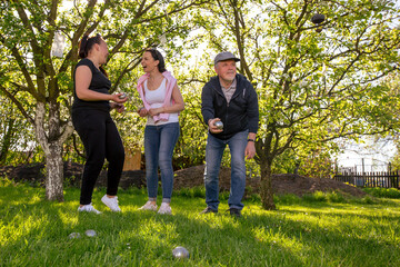 Fototapeta premium Glad, positive smiling family playing French traditional game petanque in the garden outside during lovely summer day, enjoying leisure time