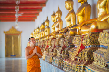 Fototapeta premium Monk walking down the hallway with buda statues around him