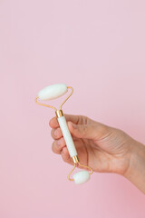 White quartz massager on a woman's hand on a pink background, massager to tighten the skin on the face and neck to eliminate wrinkles and aging effects, taking care of your health, facial skin care