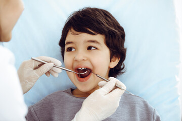 Cute arab boy sitting at dental chair with open mouth during oral checking up with doctor. Visiting dentist office. Stomatology concept