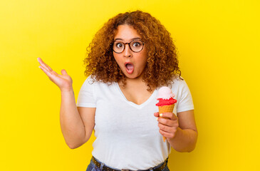 Young latin woman holding an ice cream isolated on yellow background surprised and shocked.